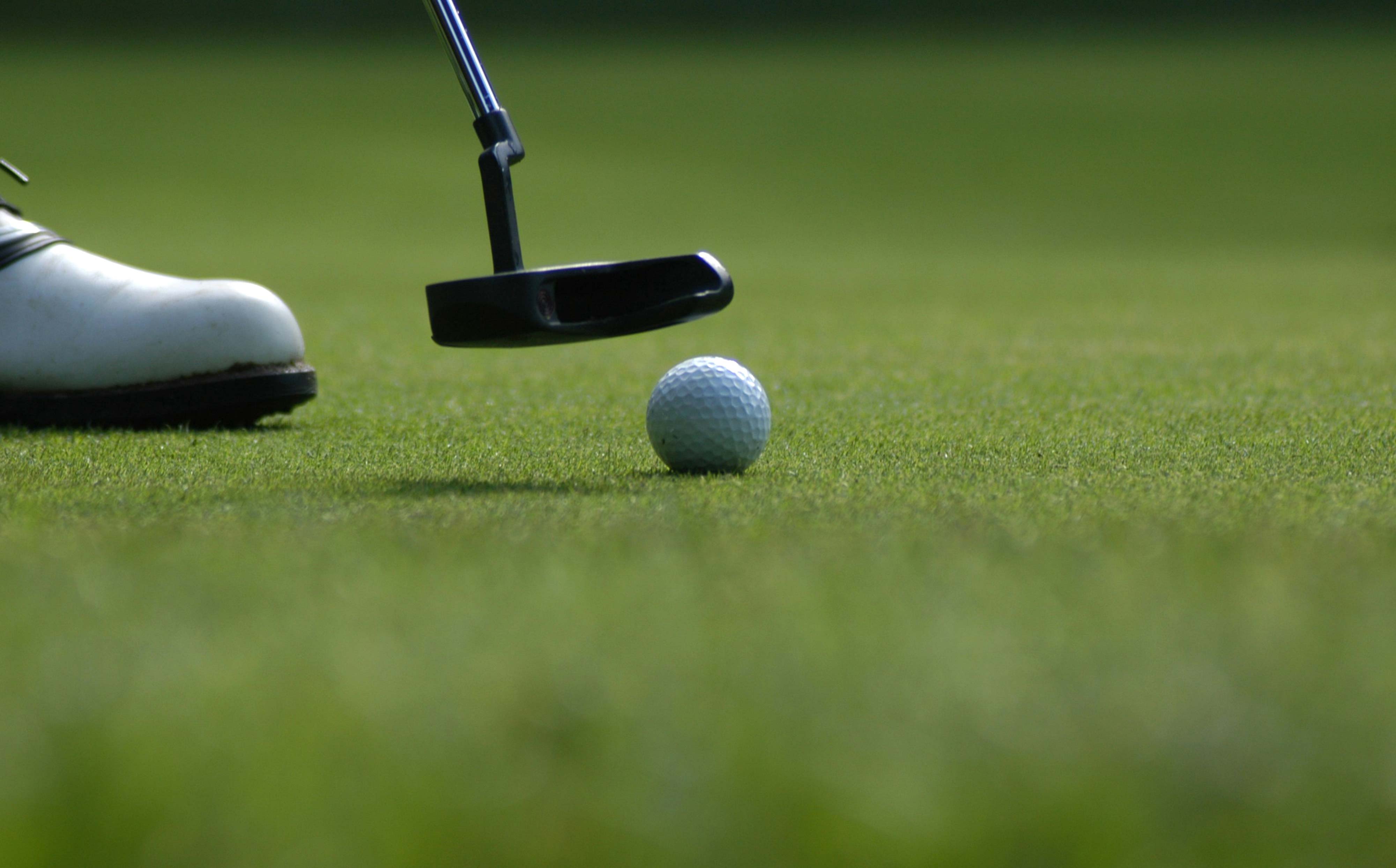 Close-up of a golfer preparing to putt a golf ball on the green, used as a hero visual for Revolution Golf.